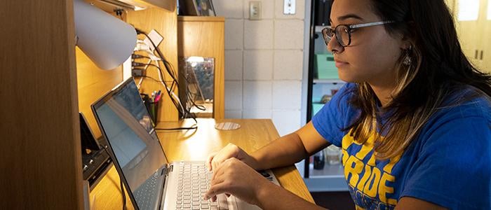 student working on laptop at desk in dorm room