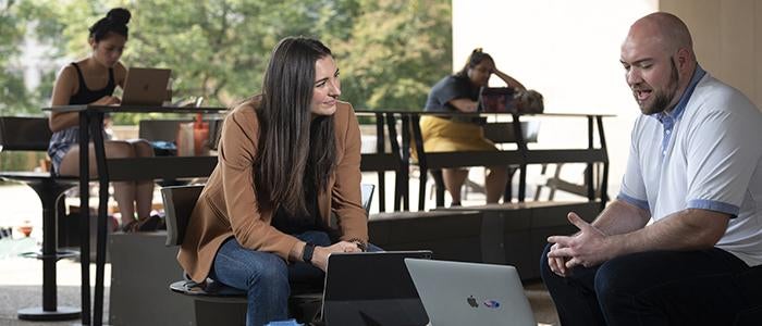 Student and advisor meeting at outdoor table with laptop