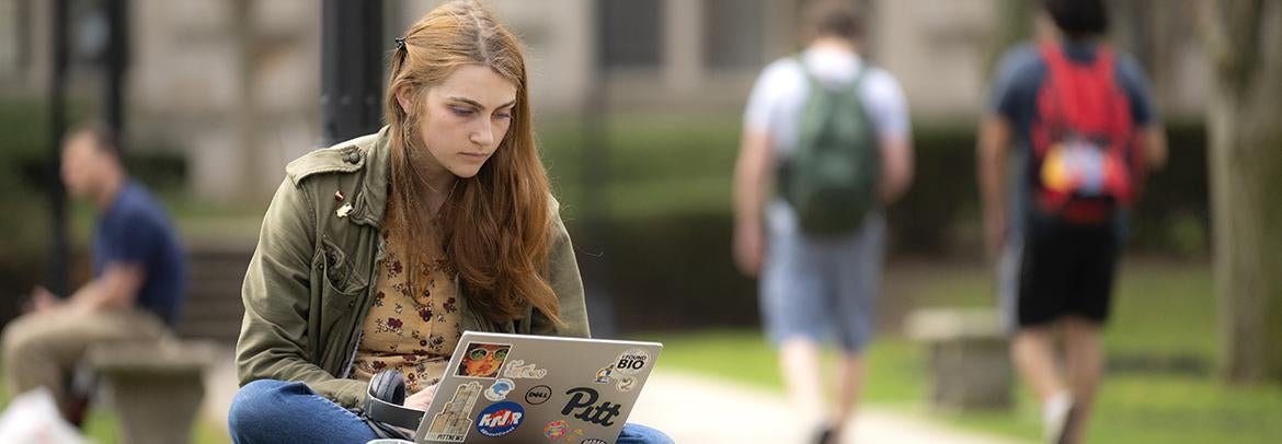 student sitting on outdoor bench using laptop