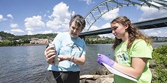 instructor and undergrad student take water samples from Mon River