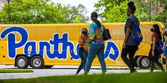 students gathered outside of bus wrapped with Panthers-themed graphic