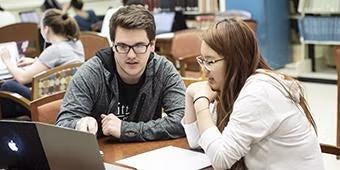 a tutor and student meet at a table with laptop and notebooks during a tutoring session in the library.
