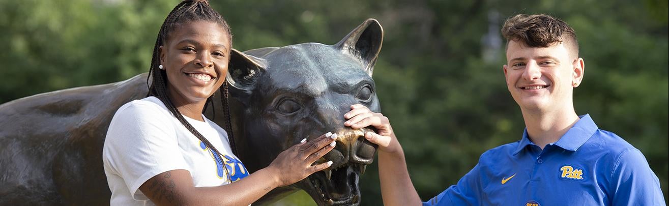 two students touching nose of Pitt's panther statue for luck